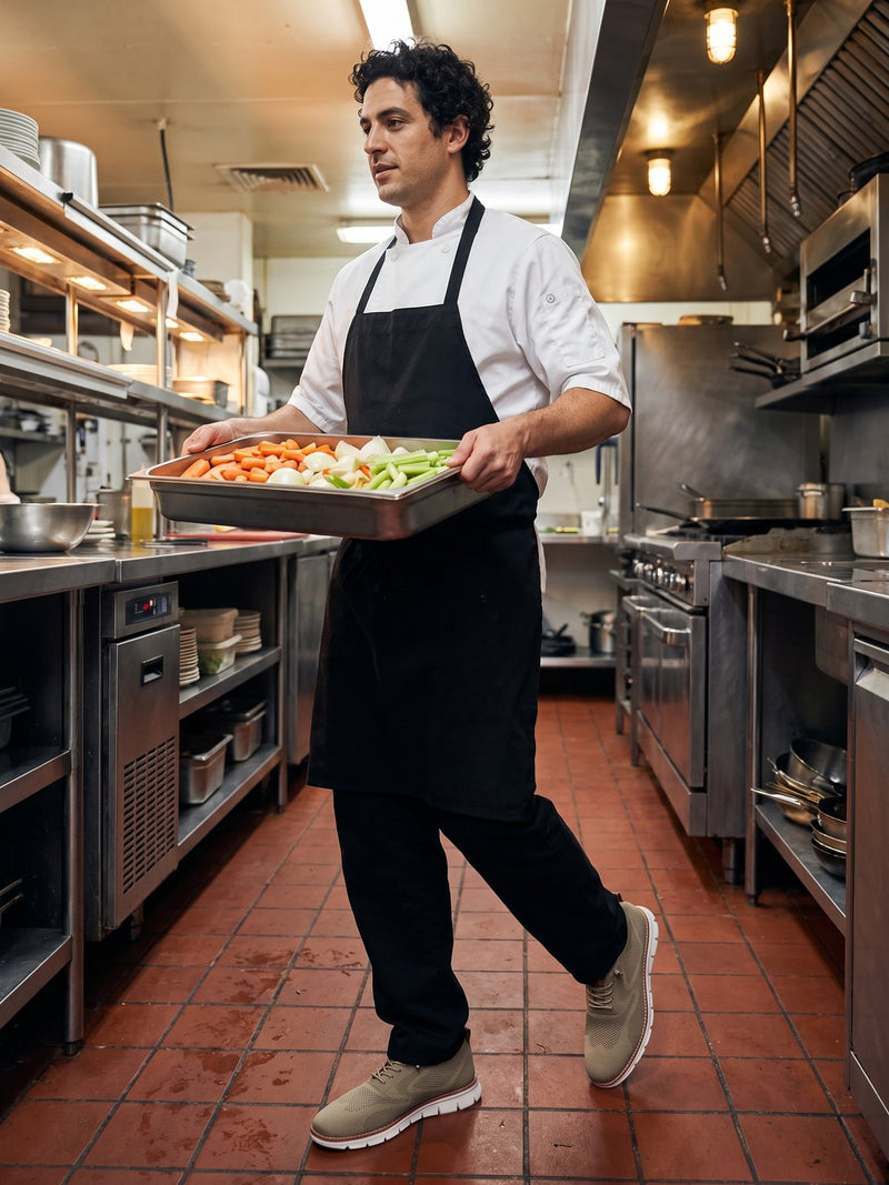 A cook carrying a tray across a kitchen wearing Again Wide